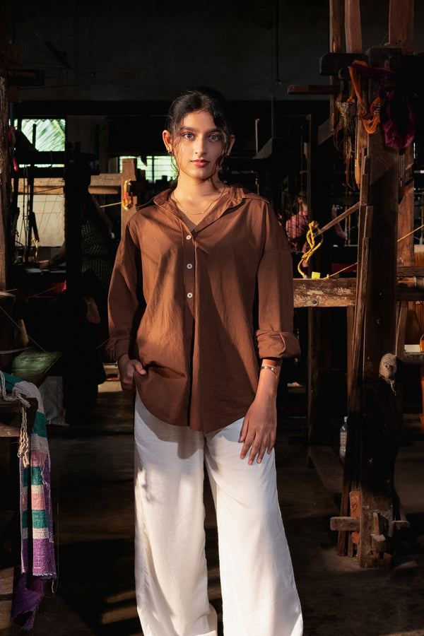 Woman wearing a brown blouse and white pants standing in a weaving shed.