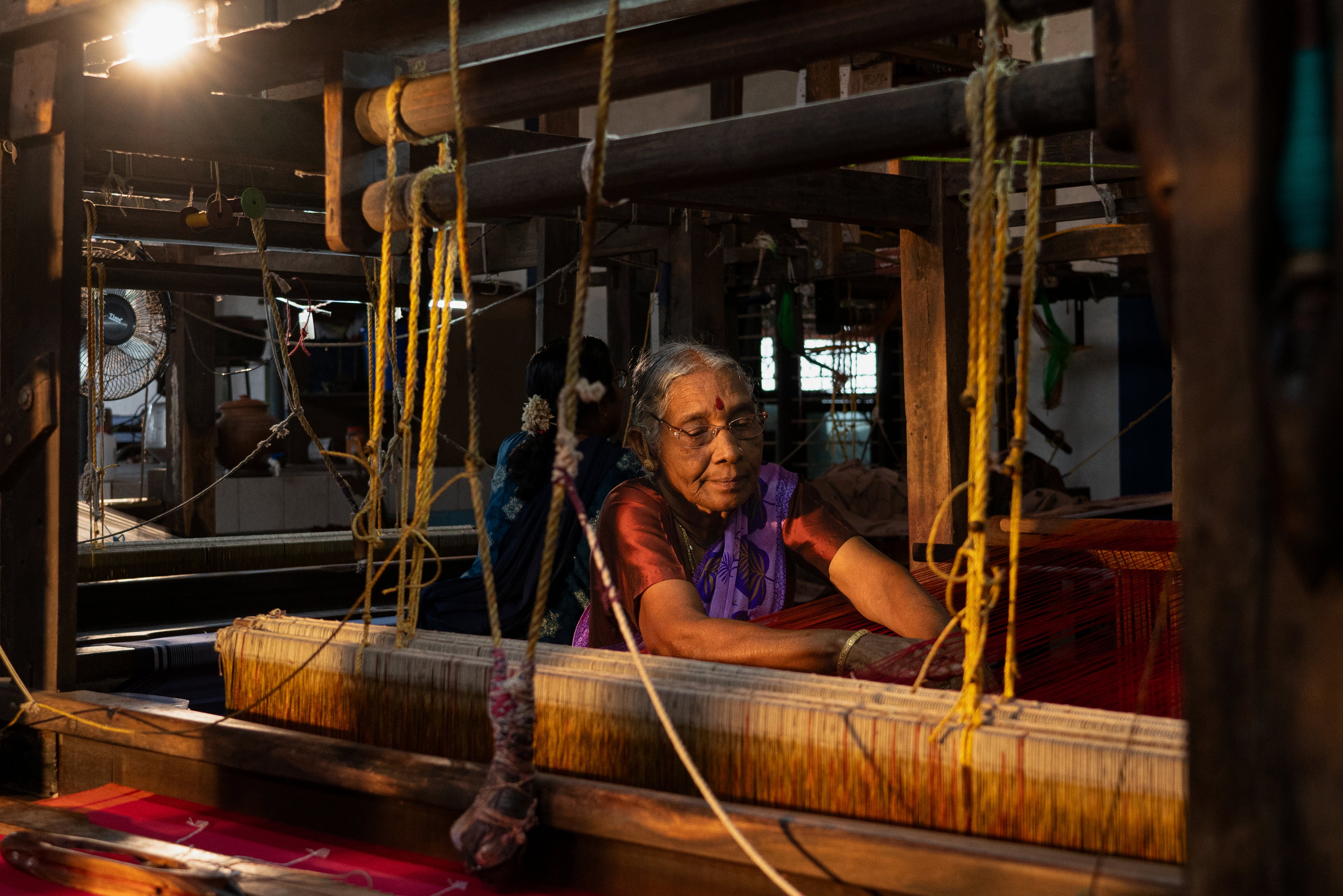 Woman operating a traditional loom in a dimly lit room