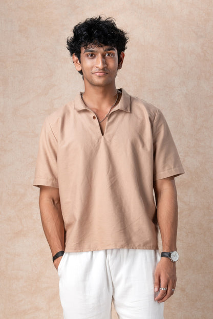 Man wearing a beige polo shirt and white pants against a beige background